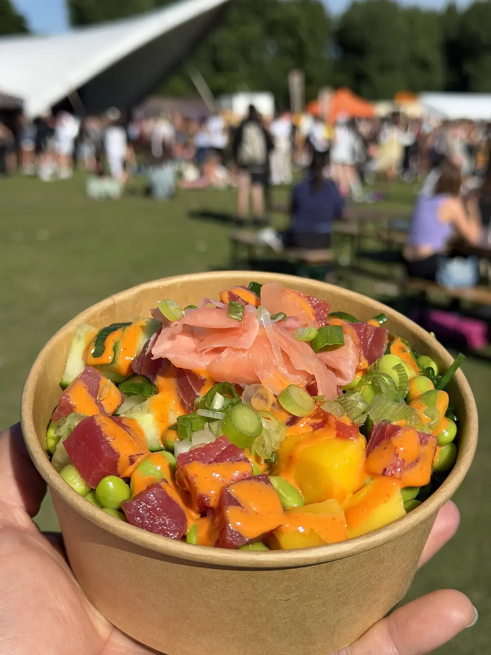 A tuna poke bowl with sriracha mayo, mango and pickled ginger held up at a busy festival