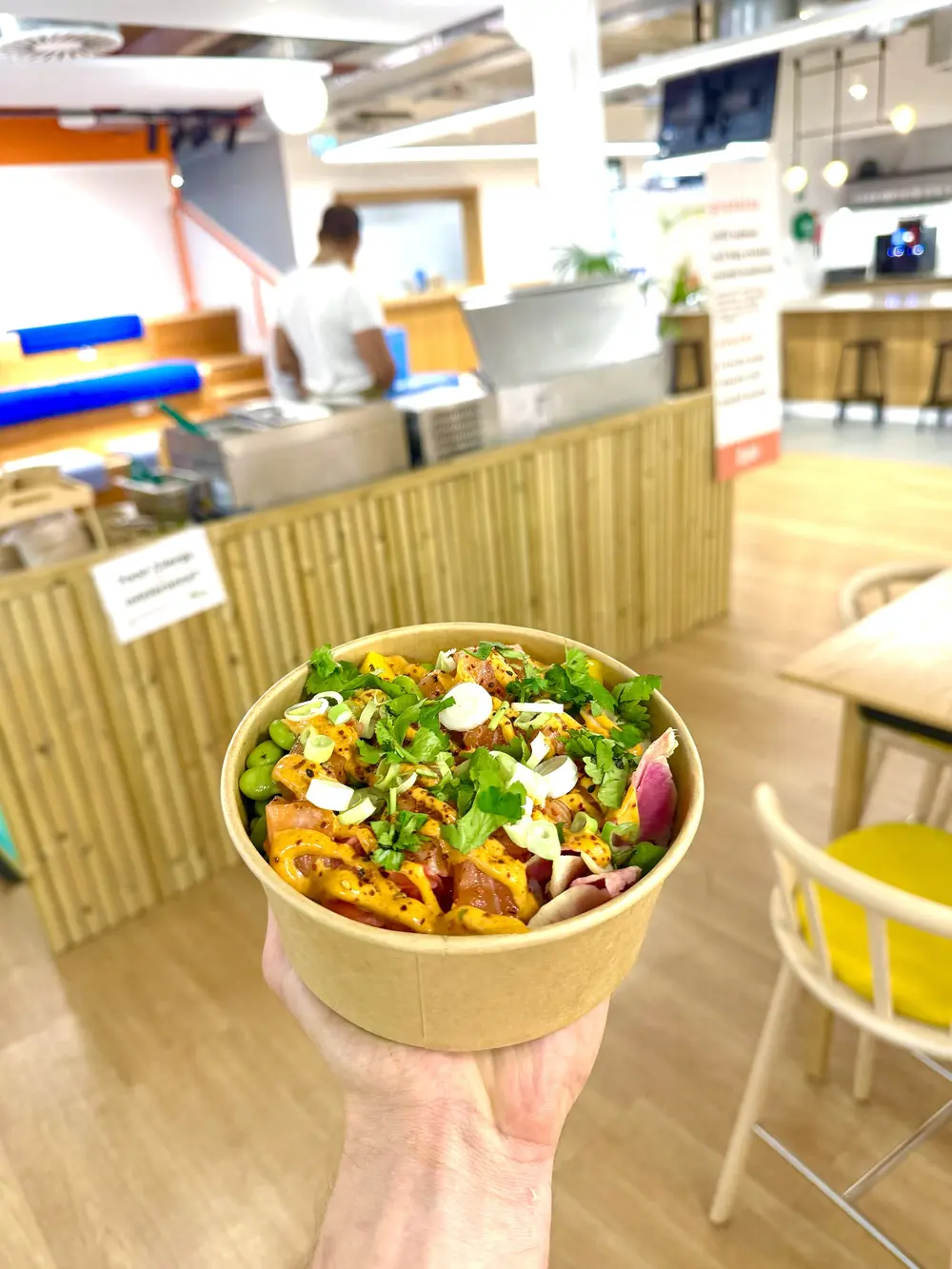 A salmon poke bowl held up in an office canteen with the Peeld counter behind